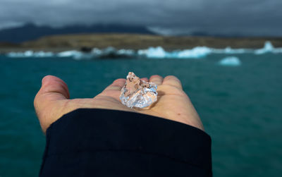 Cropped hand holding ice by sea