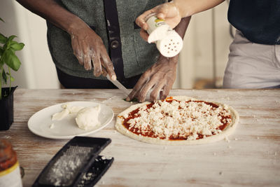 Midsection of couple preparing pizza while standing at kitchen table