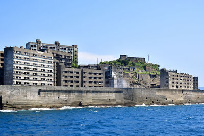 Buildings by sea against clear blue sky