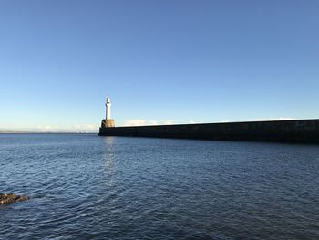 Lighthouse by sea against clear blue sky