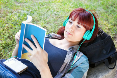 High angle view of young woman reading book while lying on field at park