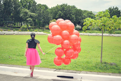 Rear view of woman holding balloons while walking on footpath at park