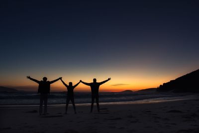 Silhouette people standing on beach against clear sky during sunset