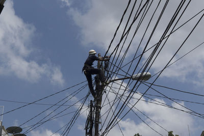Low angle view of electrician working on power line against sky