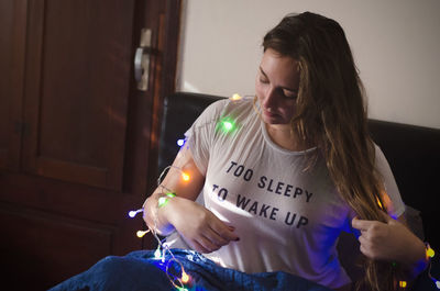 High angle view of young woman with illuminated string lights sitting on sofa at home