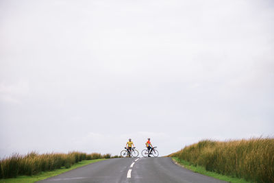 Rear view of people riding bicycle on road against sky