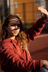 Portrait of young woman shielding eyes while sitting in sports court