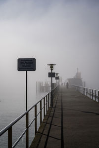 Road sign by railing against sky