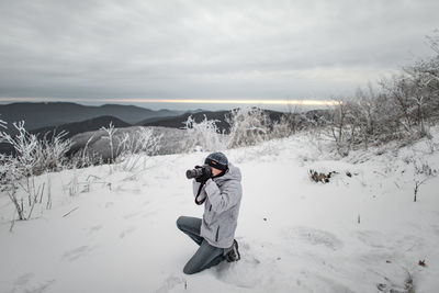 Man photographing while kneeling on snow covered landscape