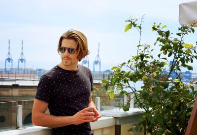 Handsome man standing on building terrace by plant against sky