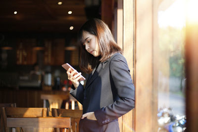 Woman holding smart phone while standing at home