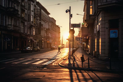 Mid distance view of silhouette man crossing road in city during sunset