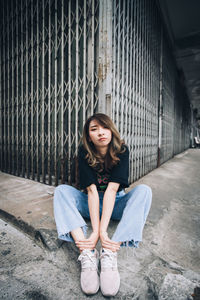 Portrait of young woman sitting against shutters