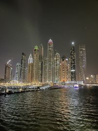 Illuminated buildings by river against sky at night