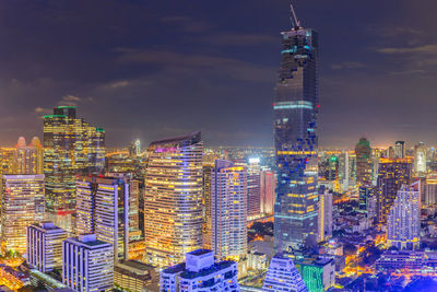 Illuminated modern buildings in city against sky at night