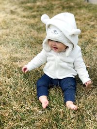 Cute baby girl wearing warm clothing sitting on grassy field