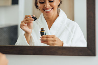 Reflection of smiling woman holding bottle seen in mirror