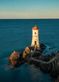 Lighthouse on rock by sea against sky
