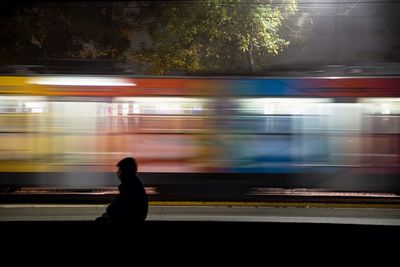 Man sitting against speeding illuminated train at night