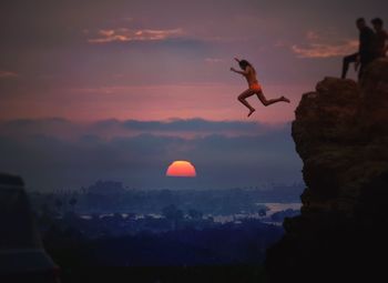 Women jumping from rock against cloudy sky