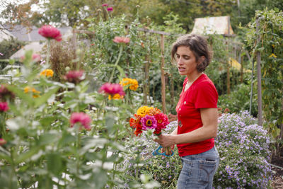 A woman stands in a beautiful flower-filled garden holding a bouquet