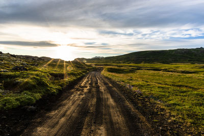 Dirt road amidst field against sky