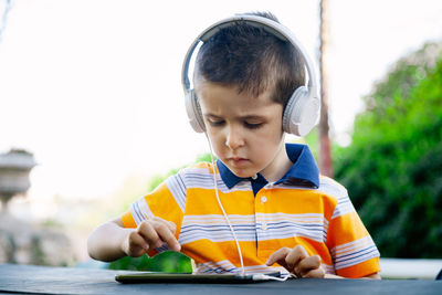 Cute boy listening music while using mobile phone against sky