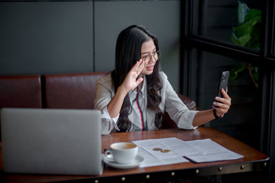 Young woman using mobile phone while sitting on table