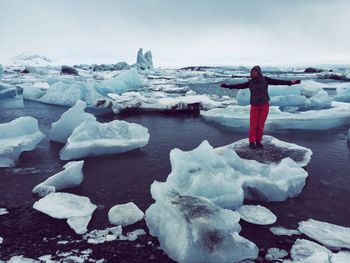 Person with arms outstretched standing on glacier at jokulsarlon