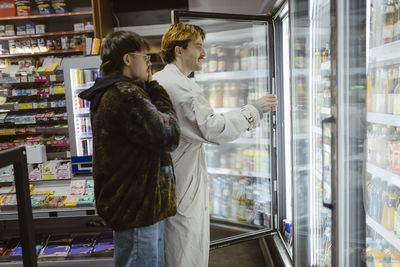 Young gay couple choosing beverages from refrigerated section while doing shopping at supermarket