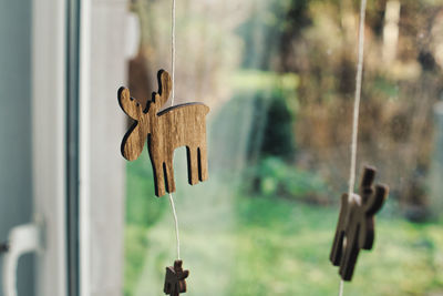 Close-up of rope with elk and moose wood decoration hanging on window while christmas
