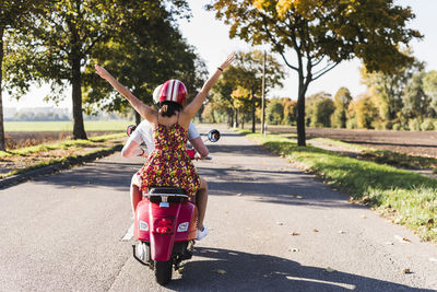 Carefree young couple riding motor scooter on country road