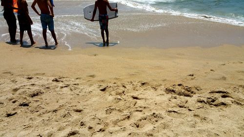 Low section of surfer in wetsuit holding surfboard on sandy beach