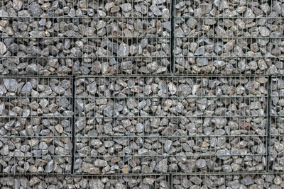 Protective gabions with grey broken stones behind grid as solid fence and solid wall and decorative