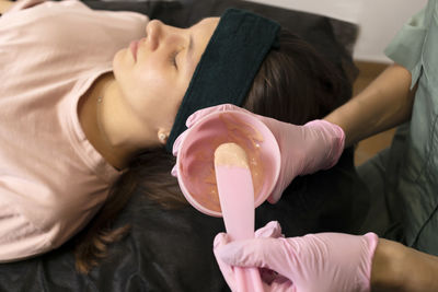 Beautician applying pink alginate mask on female, teenage girl face with smooth soft skin in beauty