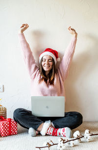 Smiling young woman with laptop while sitting by christmas gift at home