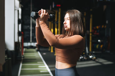 Young brunette woman training her muscles with dumbbells in the fitness club gym