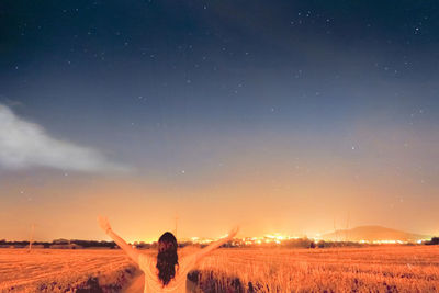 Rear view of young woman with arms outstretched standing at farm against sky