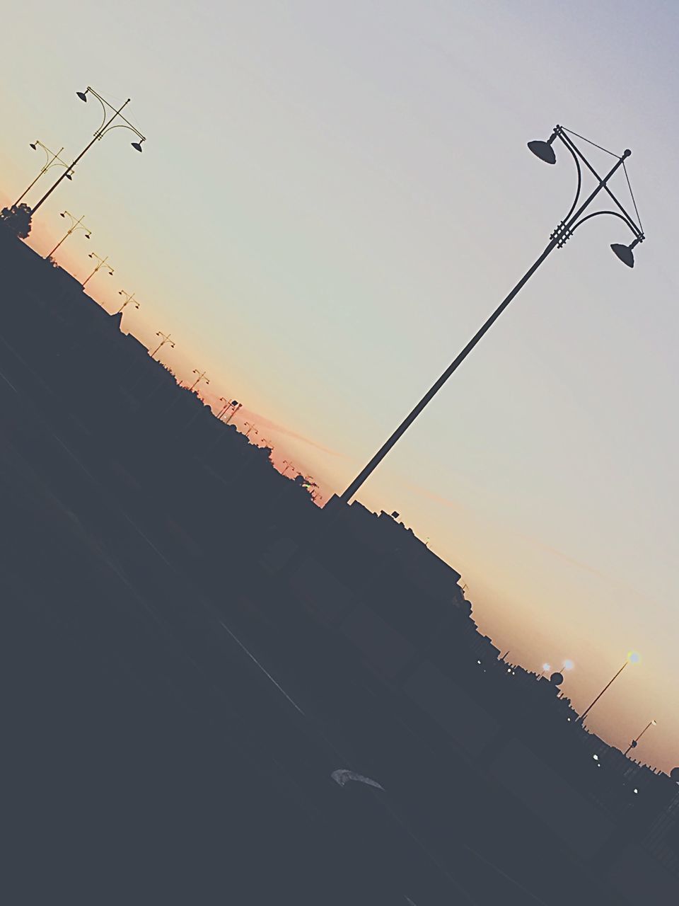 low angle view, architecture, built structure, clear sky, building exterior, sunset, silhouette, copy space, sky, street light, power line, cable, outdoors, roof, dusk, no people, connection, building, high section, orange color