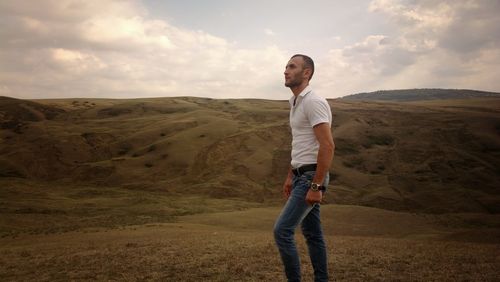 Side view of young man standing against sky on land