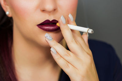 Midsection of young woman smoking cigarette against gray background