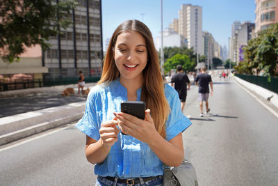 Portrait of young woman using mobile phone in city