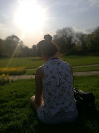 Rear view of woman sitting on field against sky