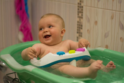 Cheerful naked baby girl sitting in bathtub at home