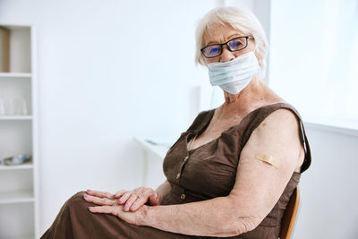 Portrait of senior woman wearing mask while sitting at hospital