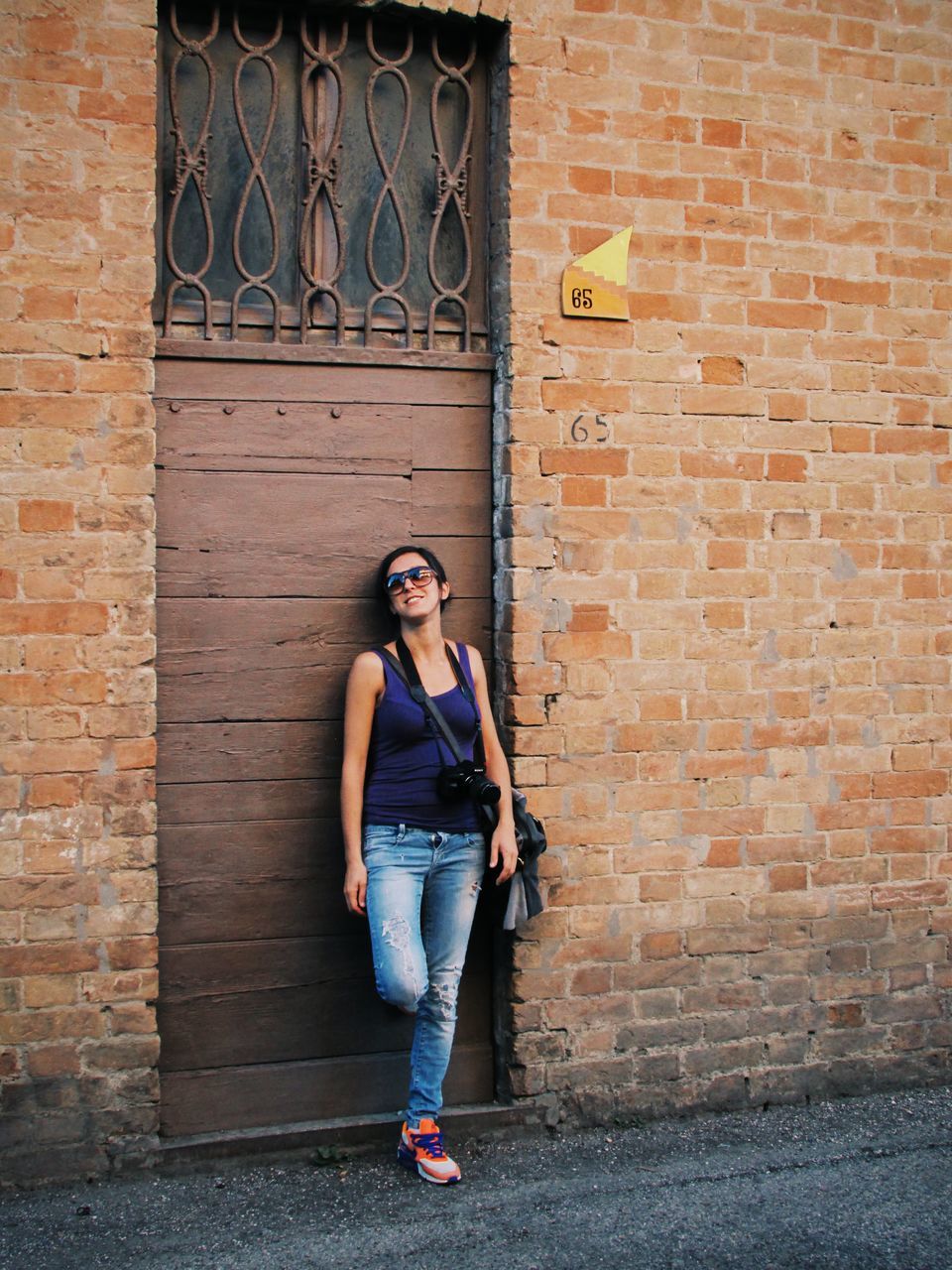 person, casual clothing, brick wall, looking at camera, architecture, building exterior, front view, portrait, lifestyles, built structure, full length, young adult, standing, smiling, wall - building feature, leisure activity, young women, happiness