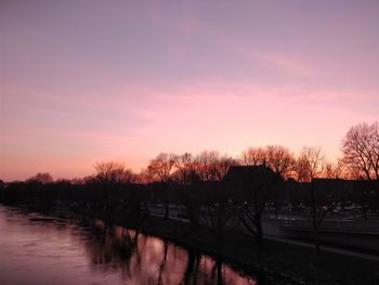 Silhouette trees by canal against romantic sky at sunset