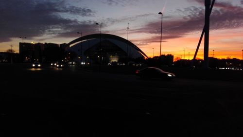 Cars on illuminated city against sky during sunset