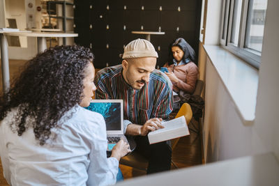 Male and female university students discussing over book while studying together