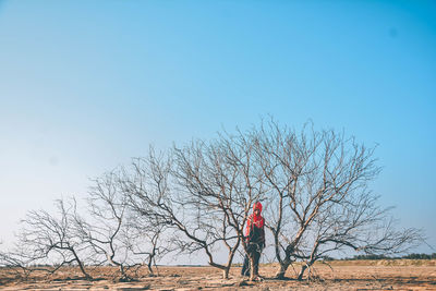 Woman standing by bare trees on land